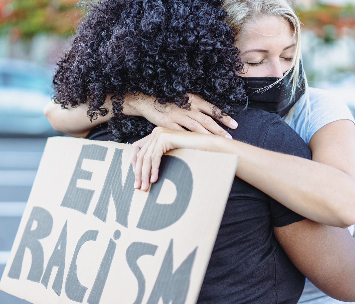 Two women hug and hold a placard reading: 'End racism'.