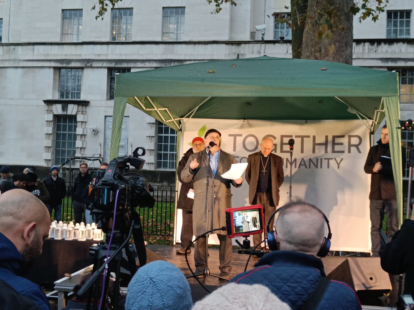 HIAS+JCORE's Executive Director David Mason stands on a stage at the Together4Humanity vigil. Behind him are stood the Archbishop of Canterbury and Imam Monawar Hussain